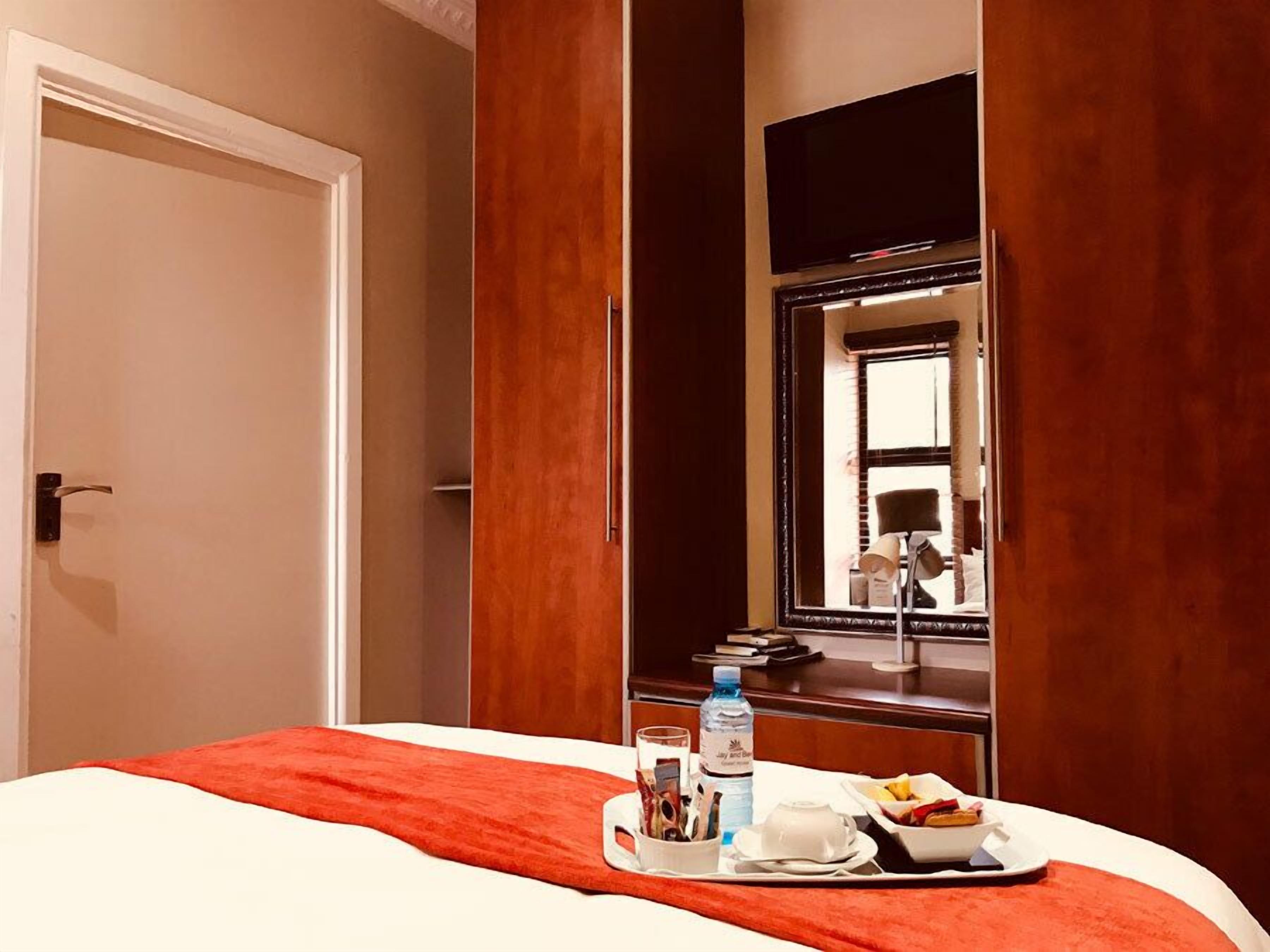 A hotel room with a bed, a tray with breakfast items, a water bottle, and a mirror reflecting the room.