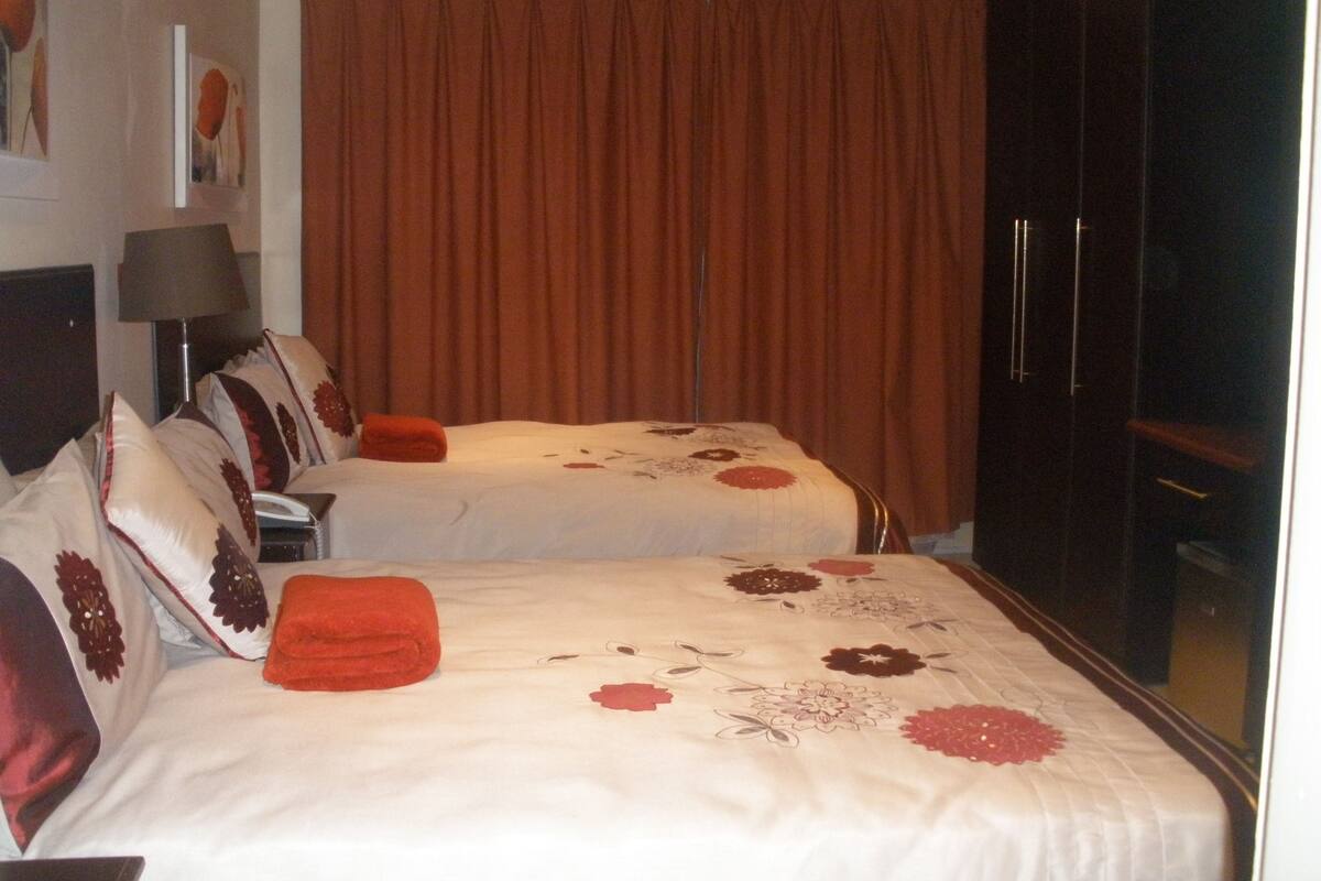 Habitación de hotel con dos camas, un ventanal con cortinas, un armario y una lámpara.