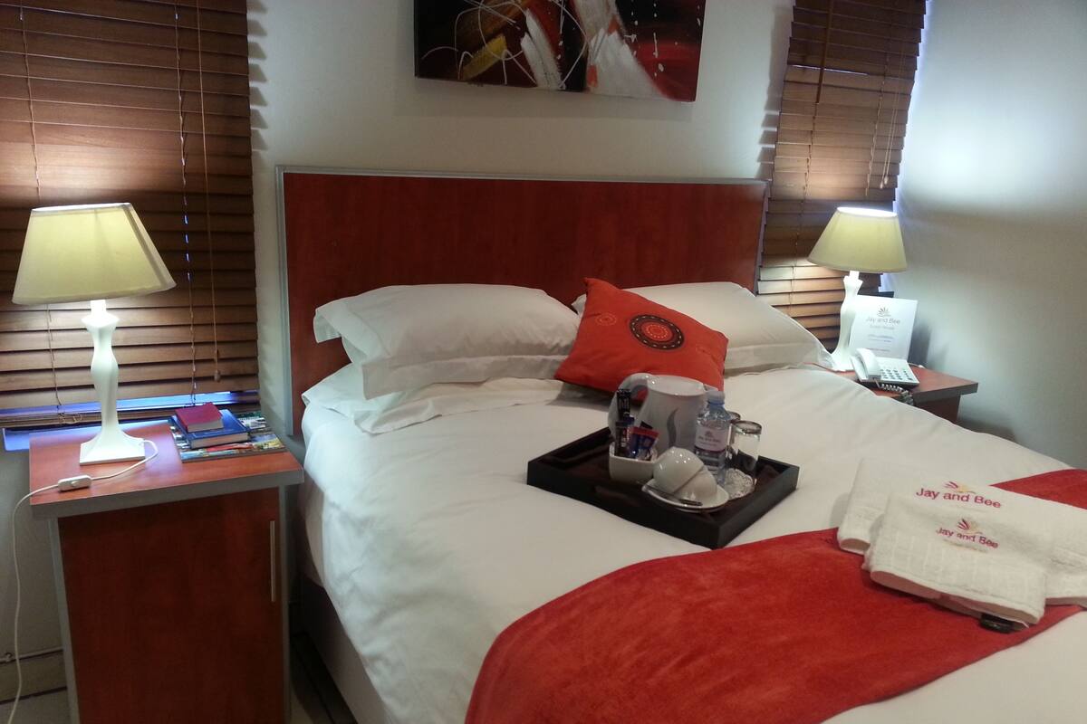 Habitación de hotel con una cama bien hecha, un frutero con artículos de aseo, un teléfono y una lámpara en la mesita de noche.