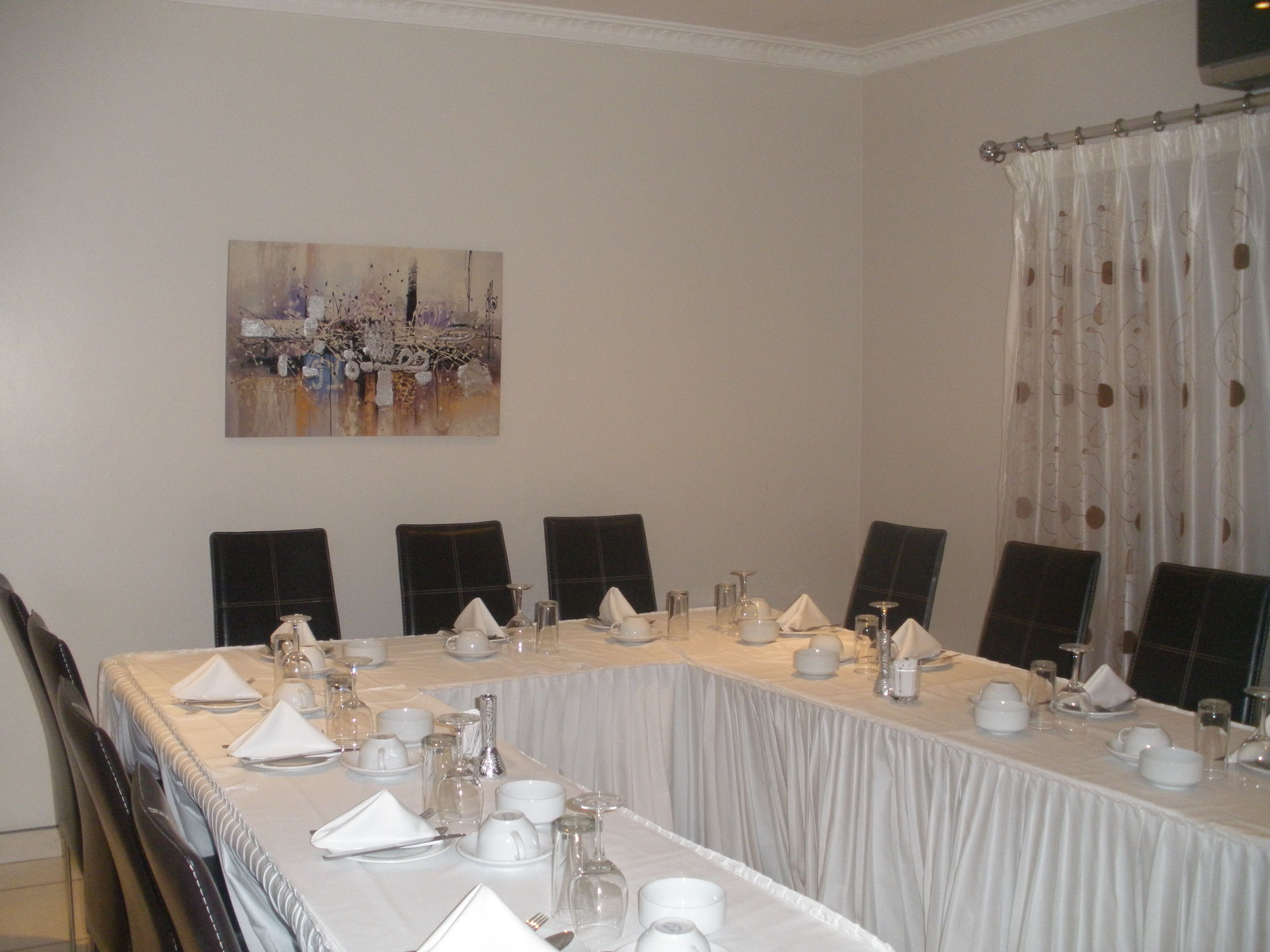 A dining table set for a meal with chairs around it, a painting on the wall, and a window with curtains.