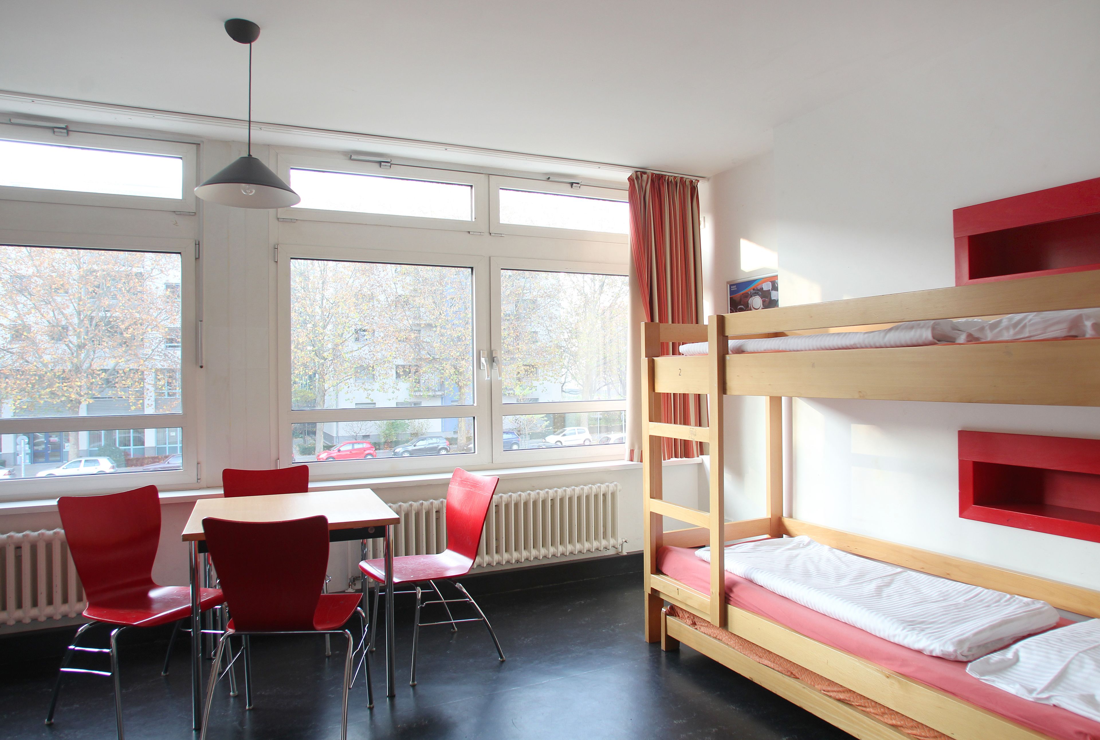 A room with bunk beds, a table, and red chairs.