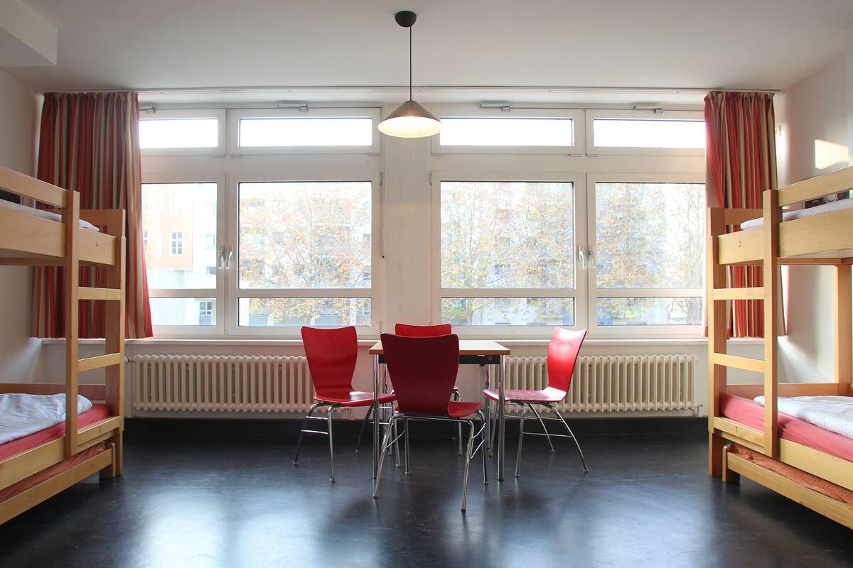 Een studentenkamer met stapelbedden, een tafel en stoelen.