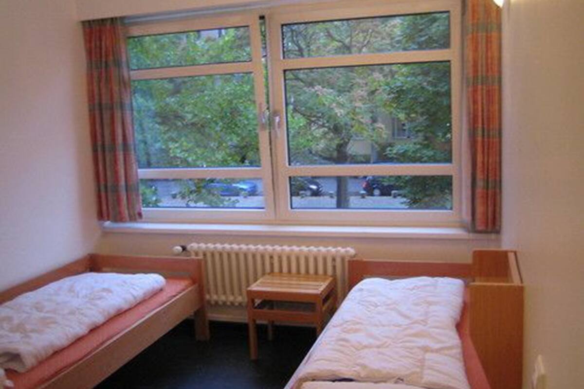 Een kamer met twee eenpersoonsbedden, een radiator en een raam met gordijnen.