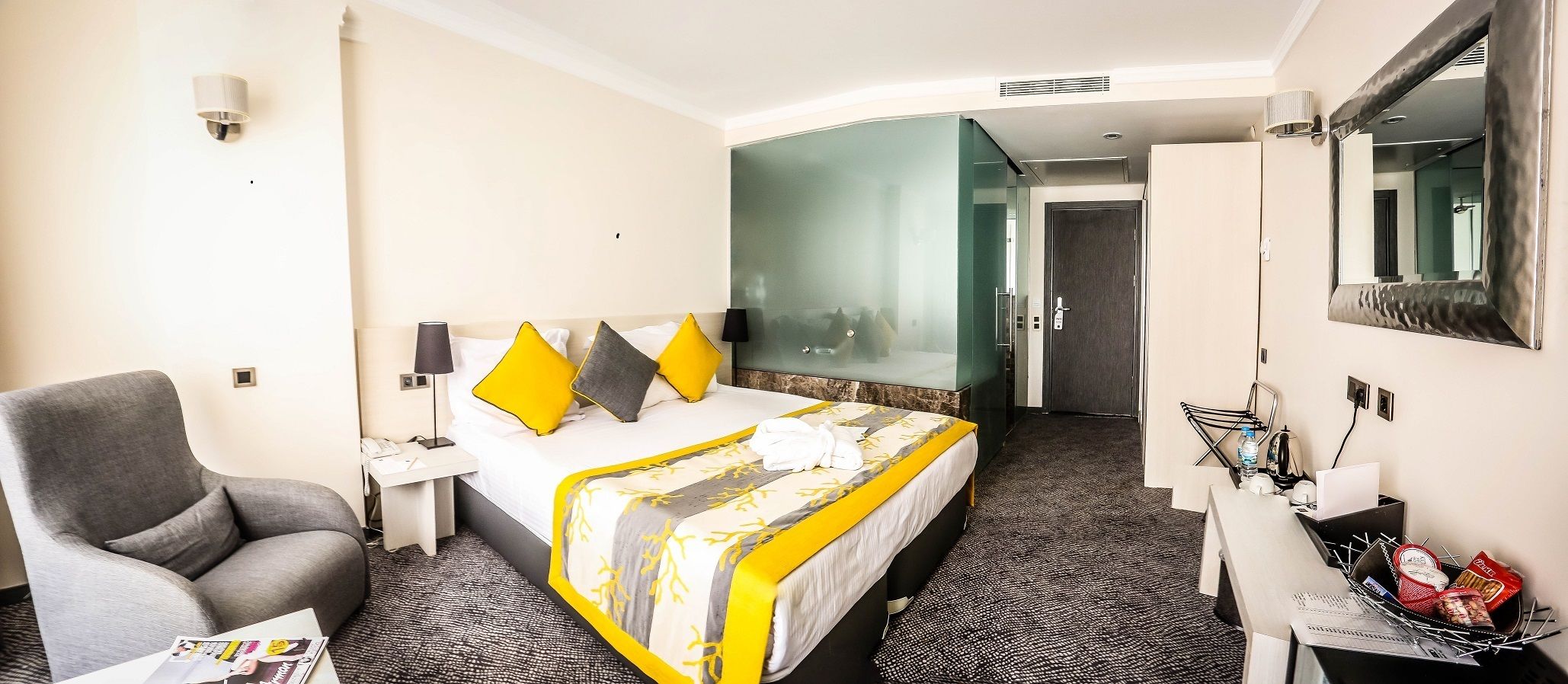 A hotel room with a bed, a desk, a chair, a mirror, and a wardrobe.