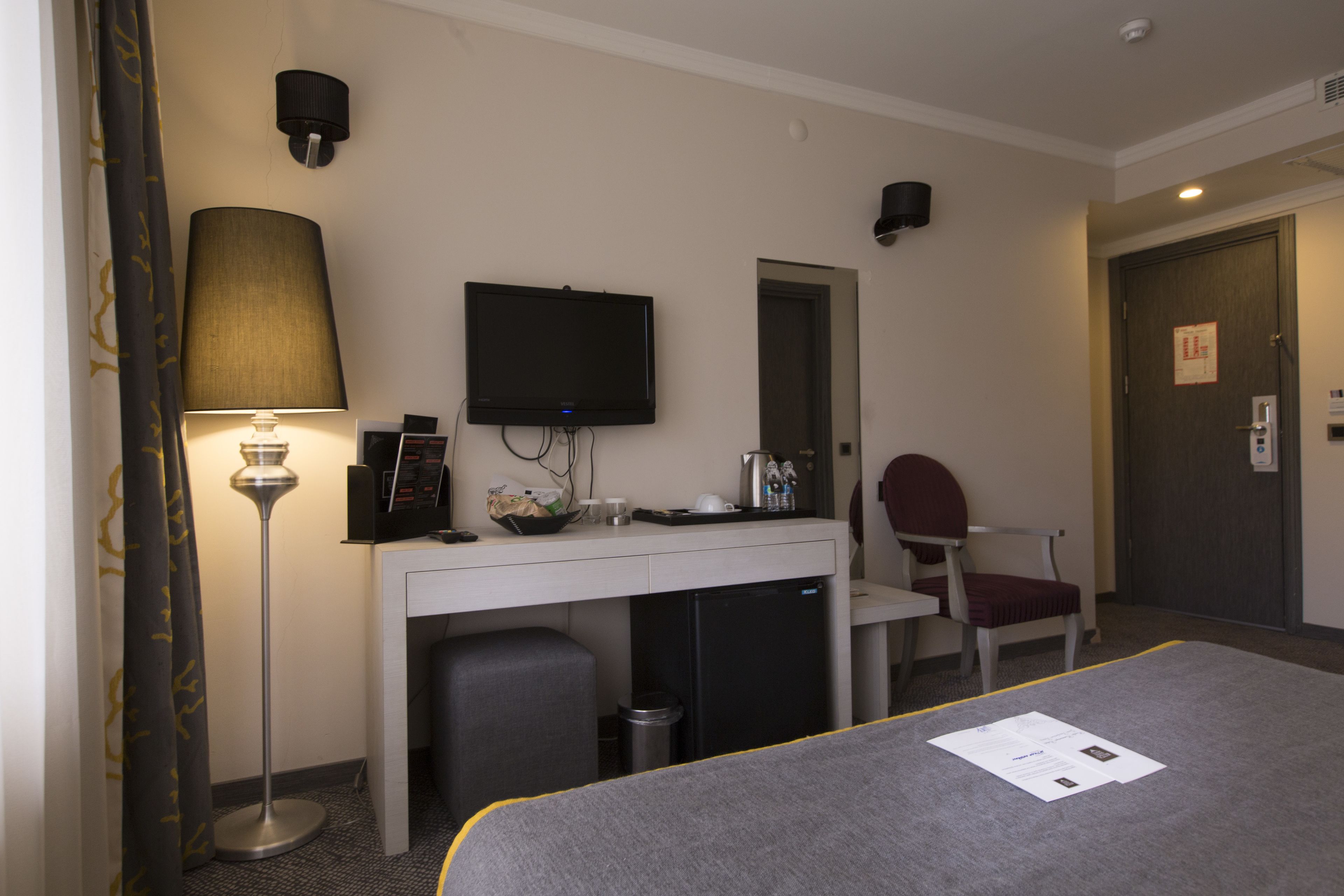 A hotel room with a bed, desk, chair, television, lamp, and a small refrigerator.