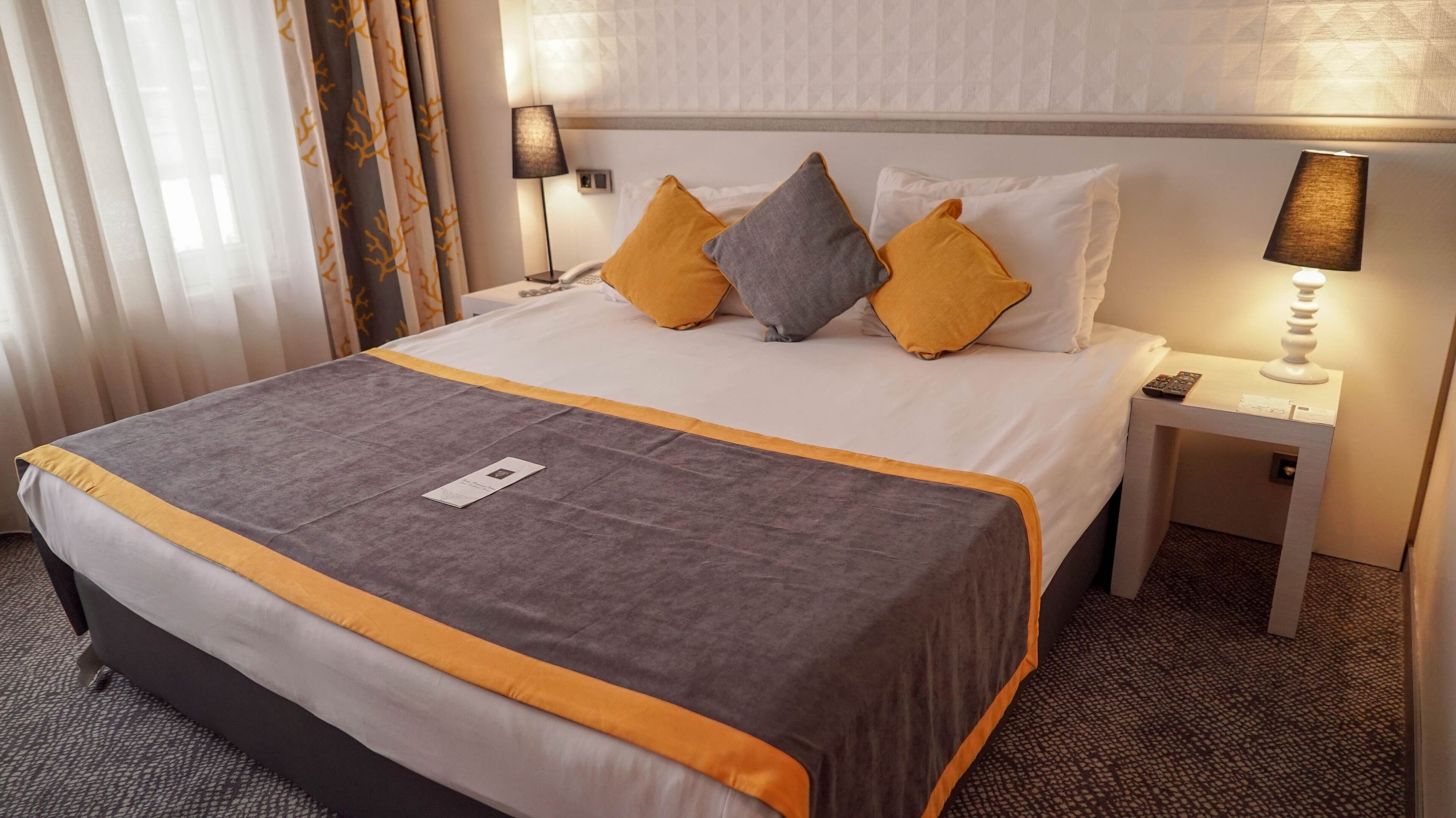 A hotel room with a large bed, two bedside tables, a lamp, and a view of the outside.