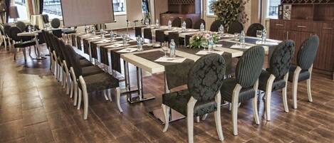 A conference room with long tables and chairs, equipped with water bottles and floral centerpieces.