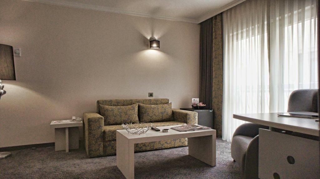 A hotel room with a sofa, a coffee table, a desk, and a lamp.