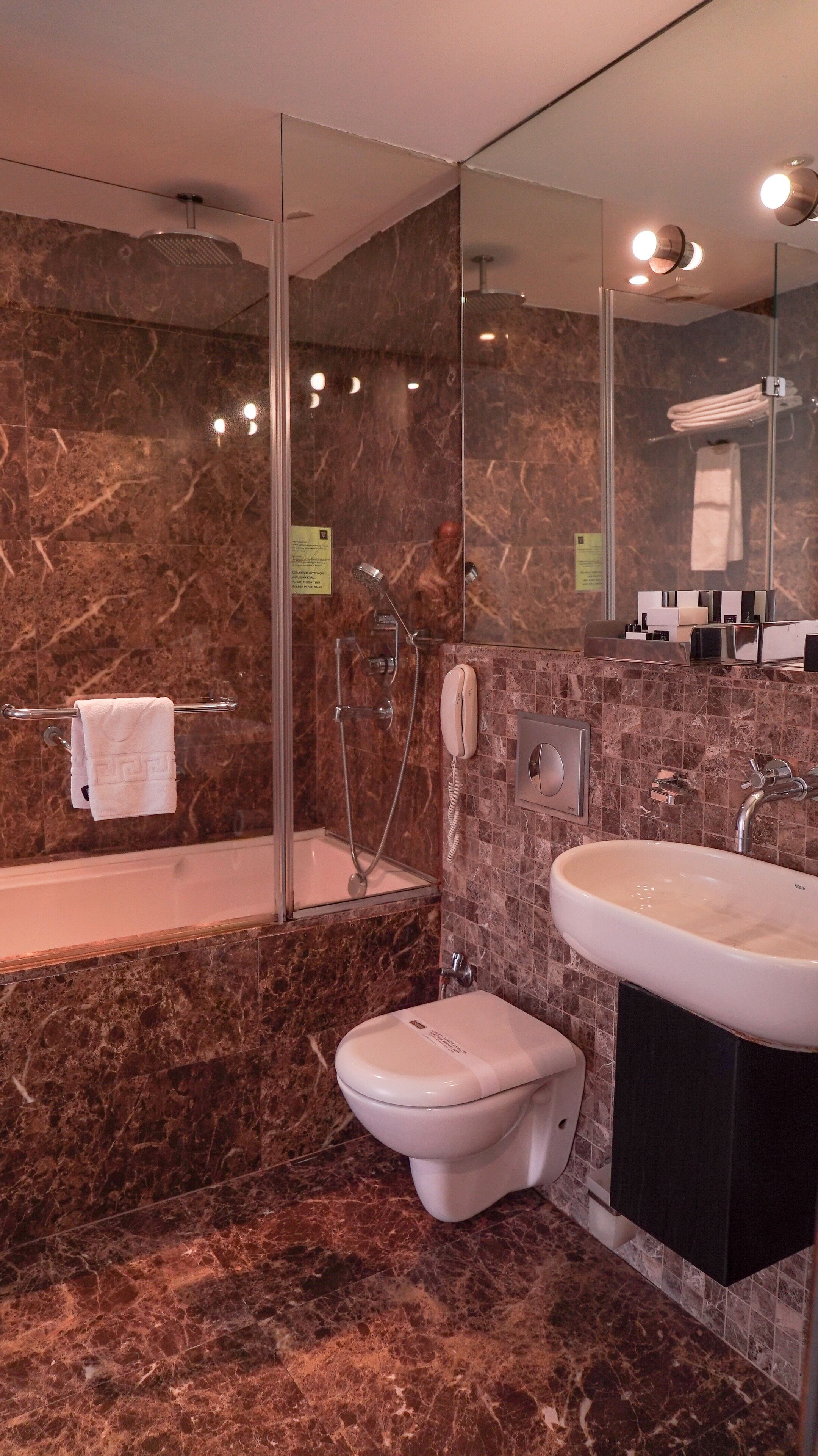 A bathroom with a marble wall, a bathtub, a toilet, and a sink.