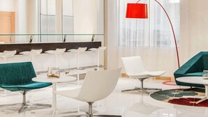 A modern lobby with a glass partition, white chairs, a red floor lamp, and a large mirror. - Ibis Yanbu Saudi Arabia (Yanbu)