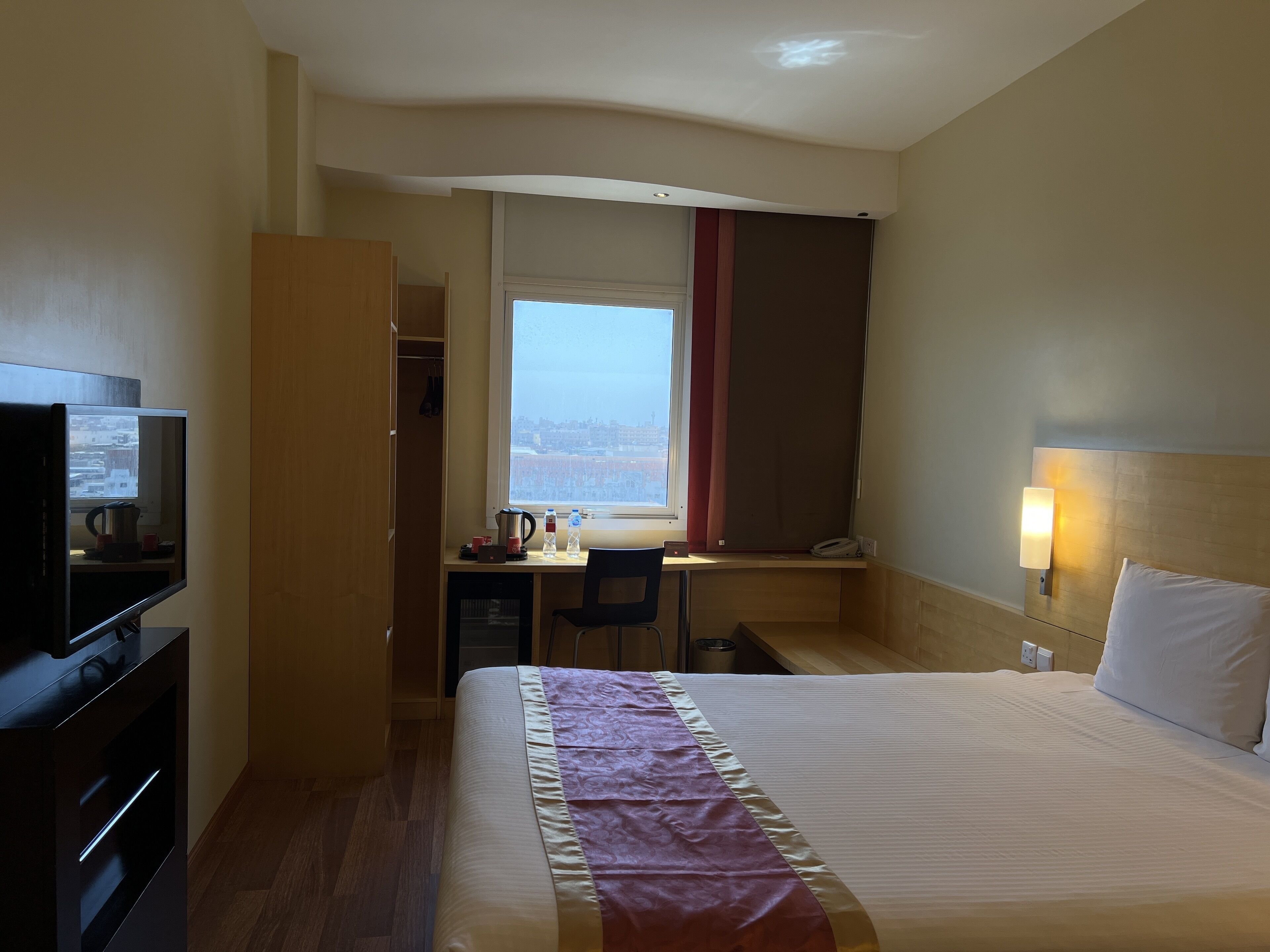 Une chambre d’hôtel avec un lit, un bureau, une télévision et une fenêtre avec des rideaux.