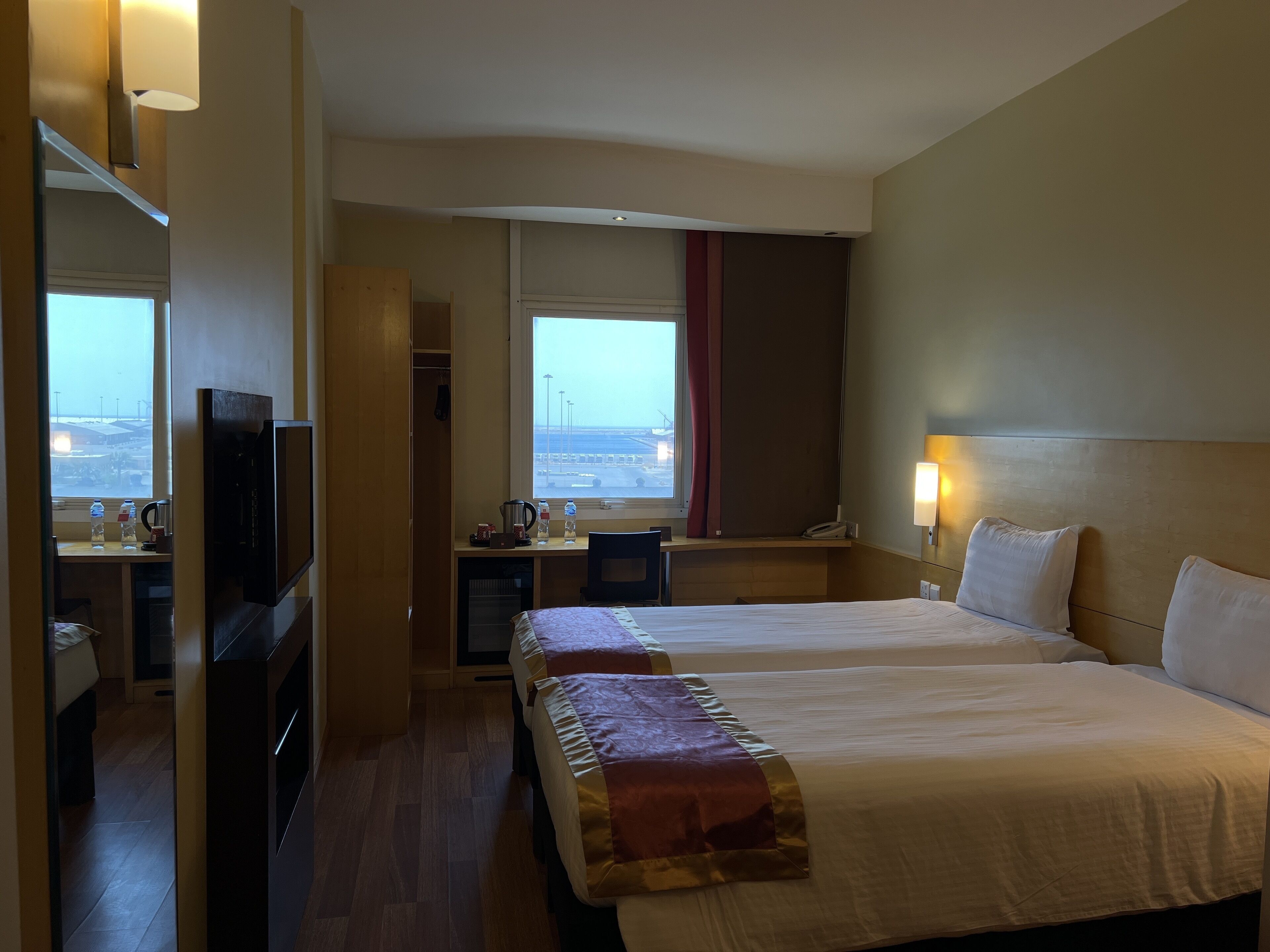Ett hotellrum med två sängar, ett skrivbord med en stol, en TV och ett fönster med utsikt över flygplatsen.