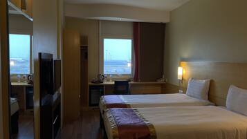 Ett hotellrum med två sängar, ett skrivbord med en stol, en TV och ett fönster med utsikt över flygplatsen.