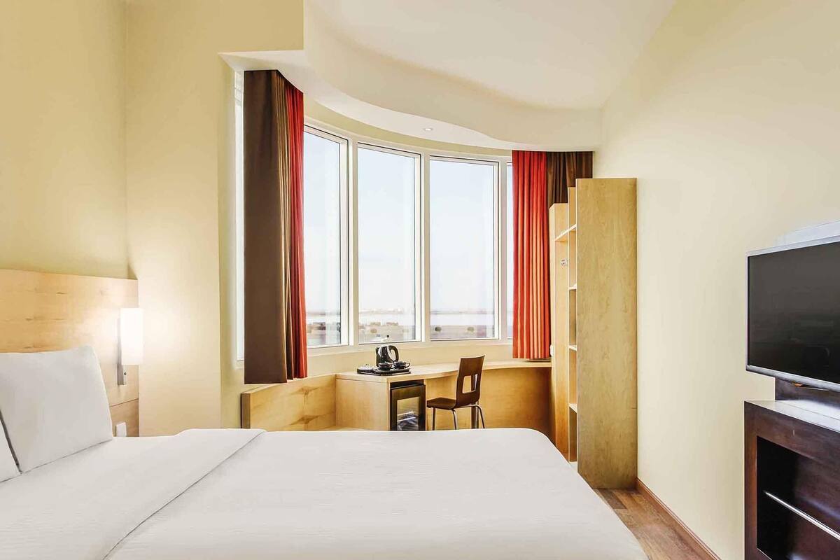 A hotel room with a bed, a desk, a chair, a TV, and a window with curtains.