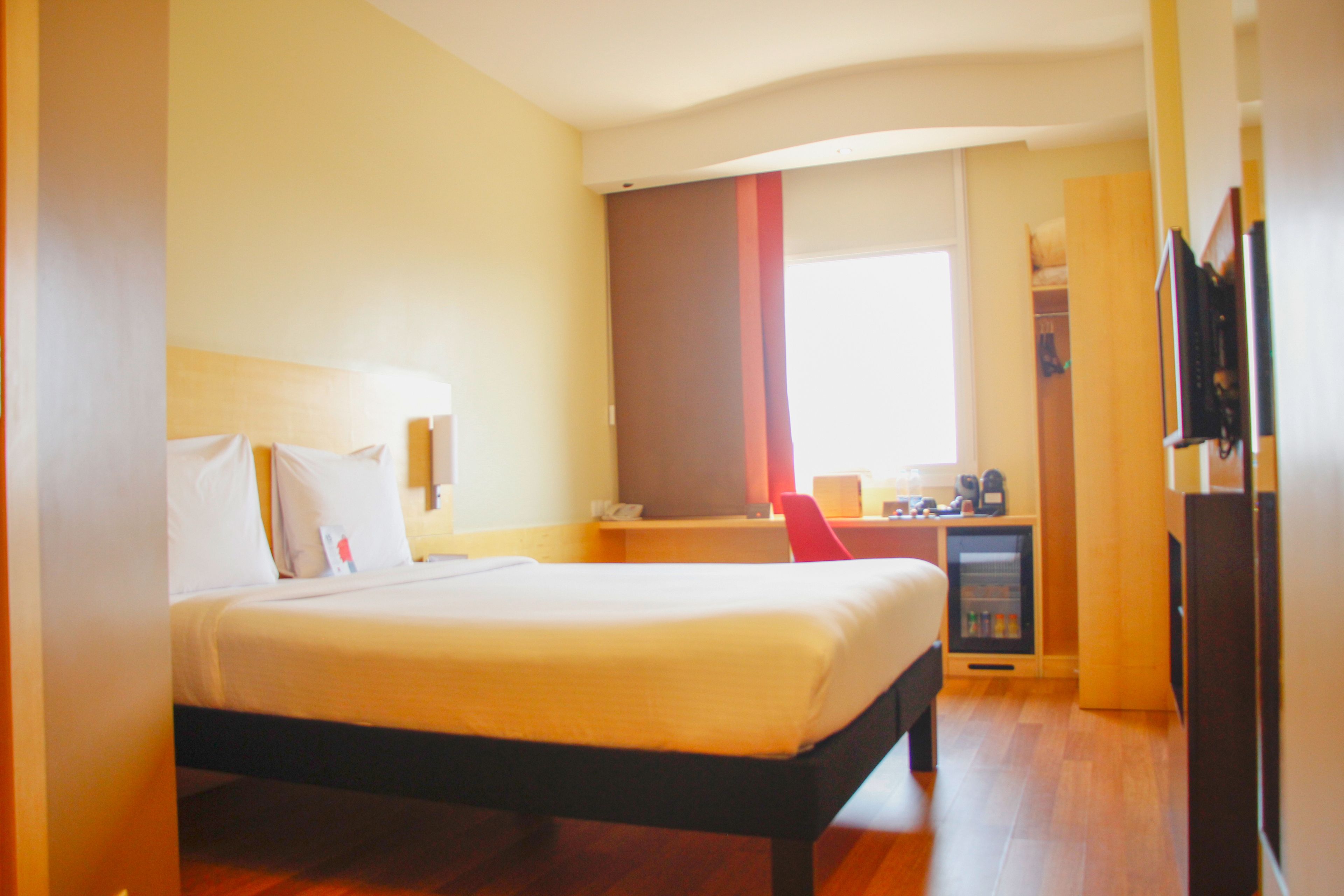 A hotel room with a bed, bedside table, and a small desk with a chair.