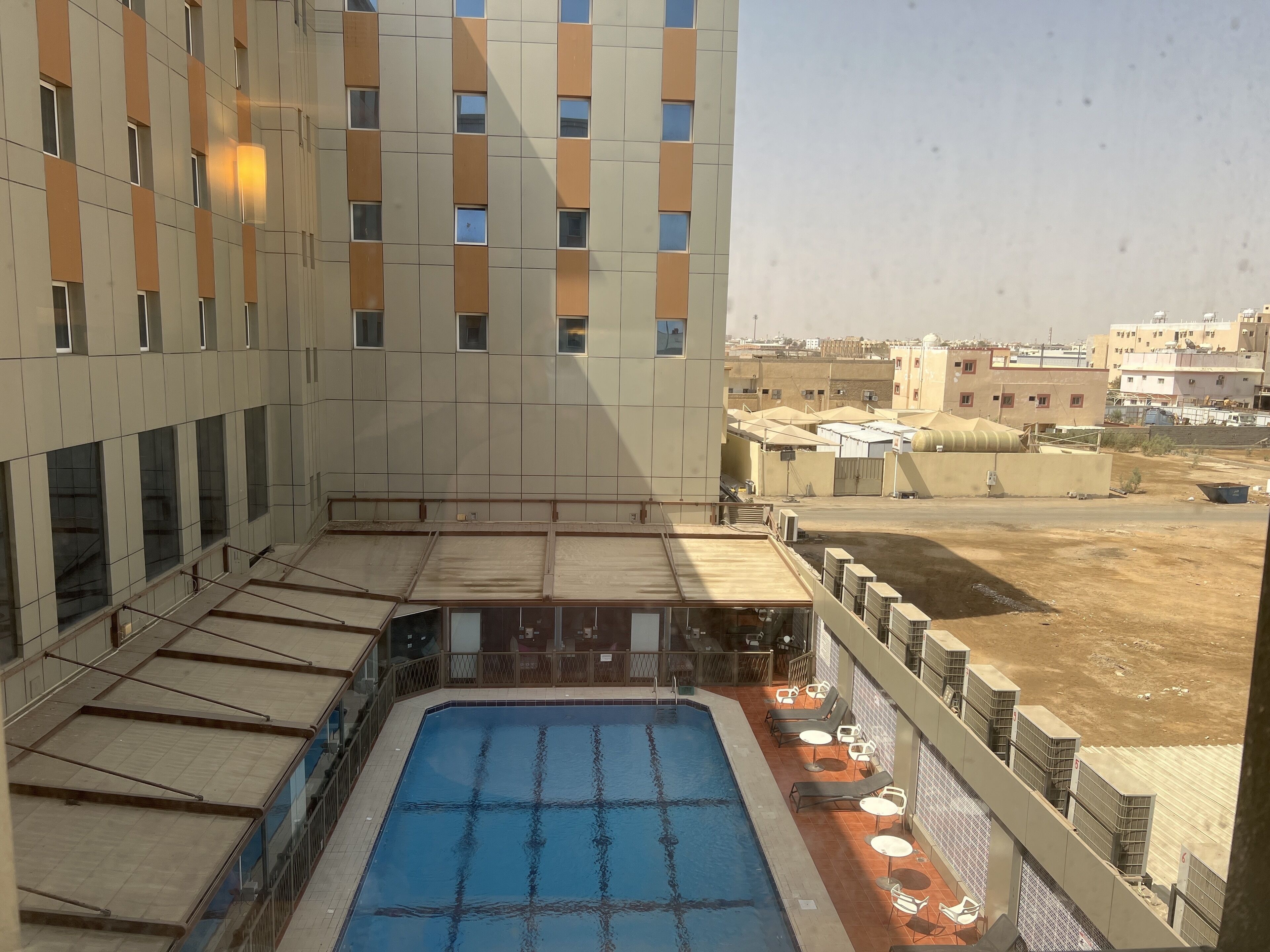 A hotel rooftop with a swimming pool, outdoor seating, and a view of the surrounding buildings.