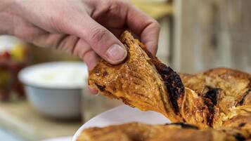 Une main tenant un morceau de viande grillée, probablement du poulet, avec des marques de cuisson, au-dessus d’une assiette de nourriture.