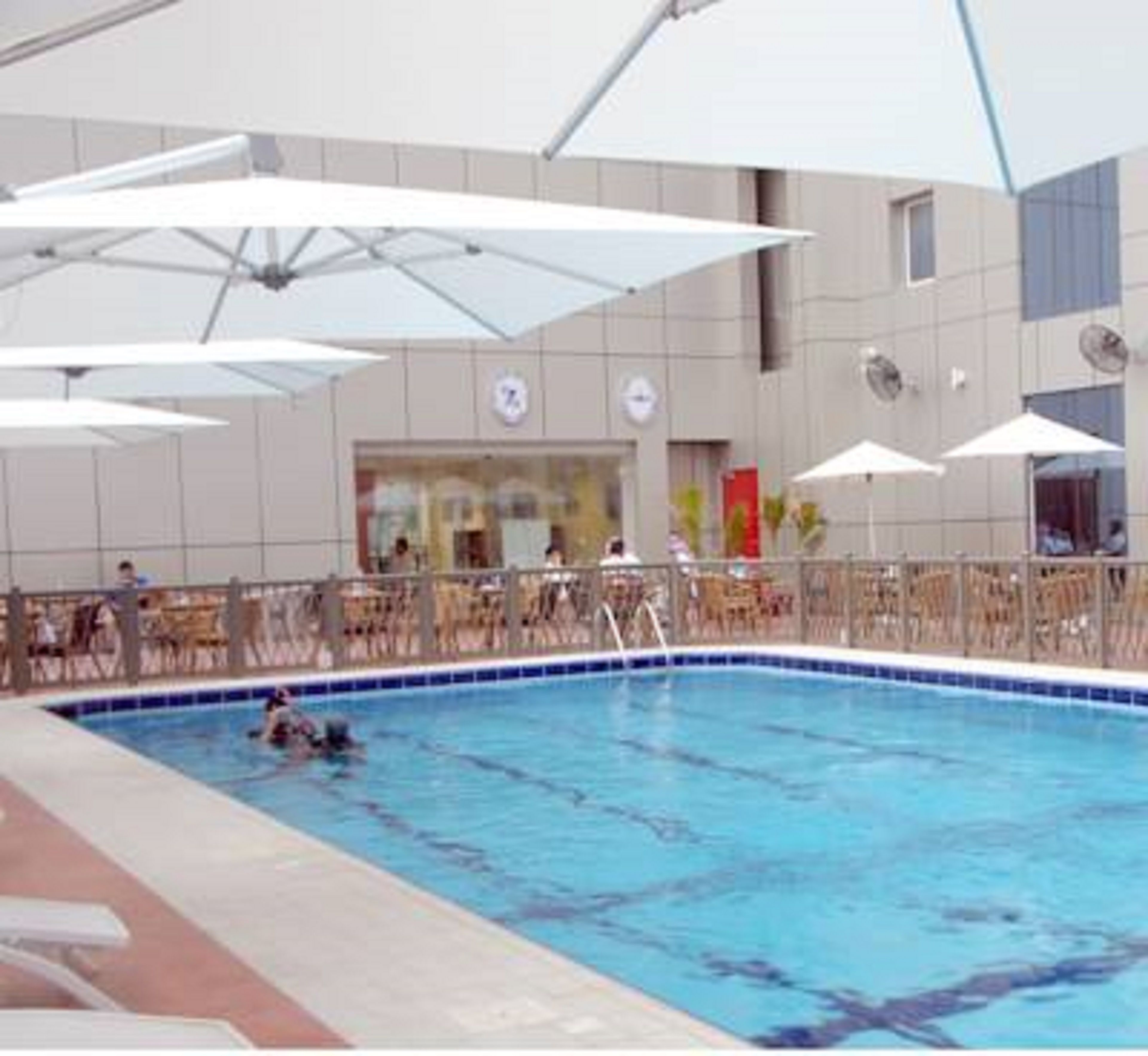 A swimming pool with umbrellas, a tiled deck, and a building with a modern design in the background.