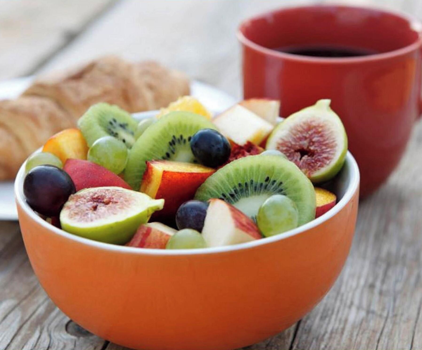 A bowl of assorted fruits and a red mug on a wooden surface.