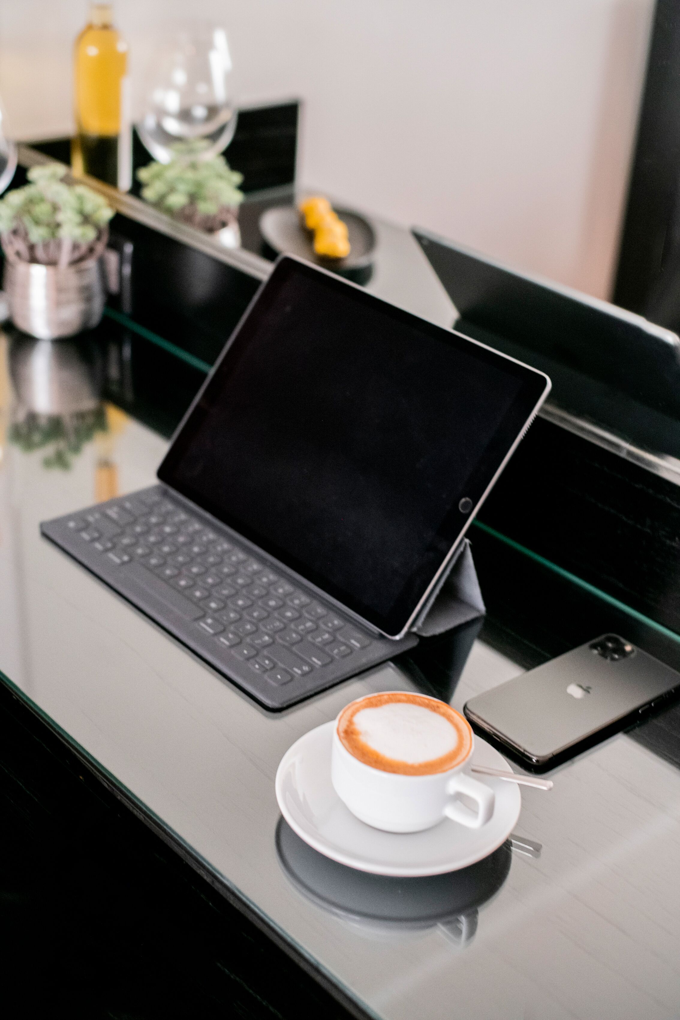 A laptop on a glass table with a cup of coffee and a smartphone beside it.