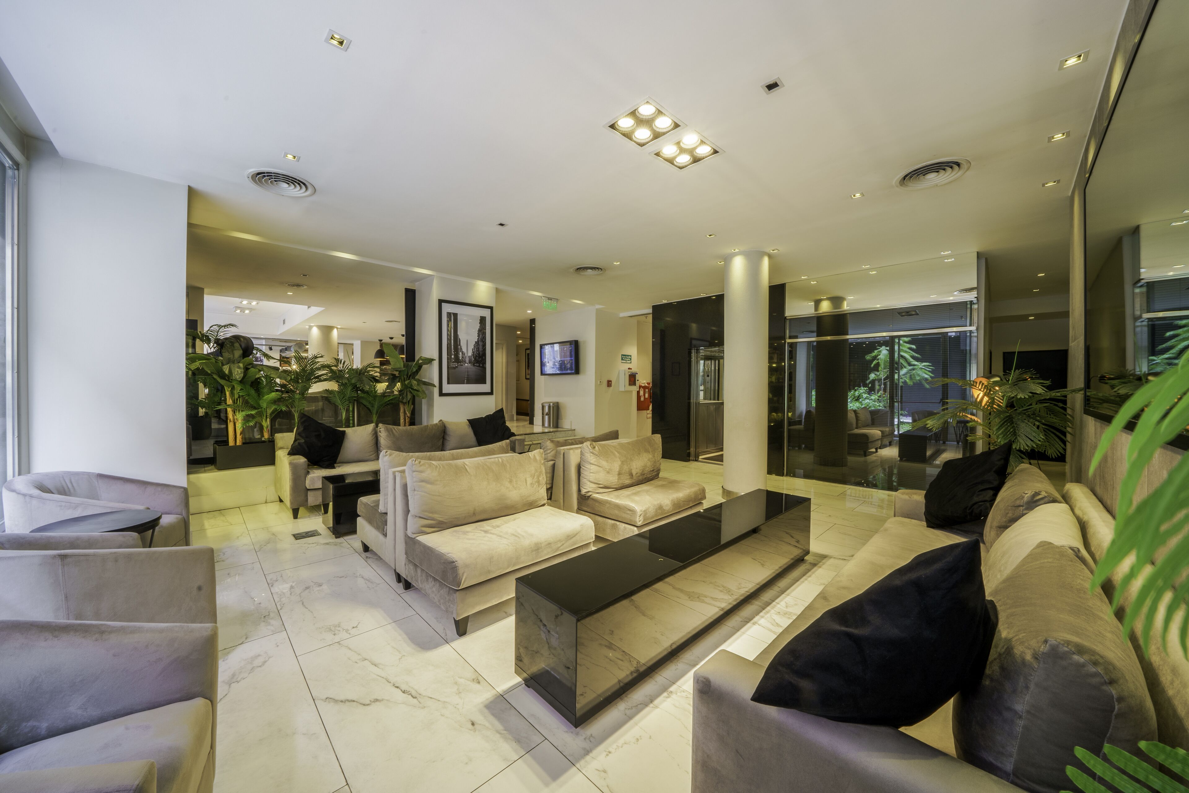 A modern hotel lobby with a spacious seating area, a flat-screen TV, and a large mirror reflecting the interior.