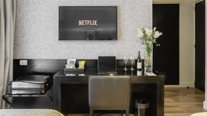 A hotel room with a desk, a laptop, a suitcase, a vase with flowers, and a television screen displaying "NETFLIX". - Principado Downtown (Buenos Aires)