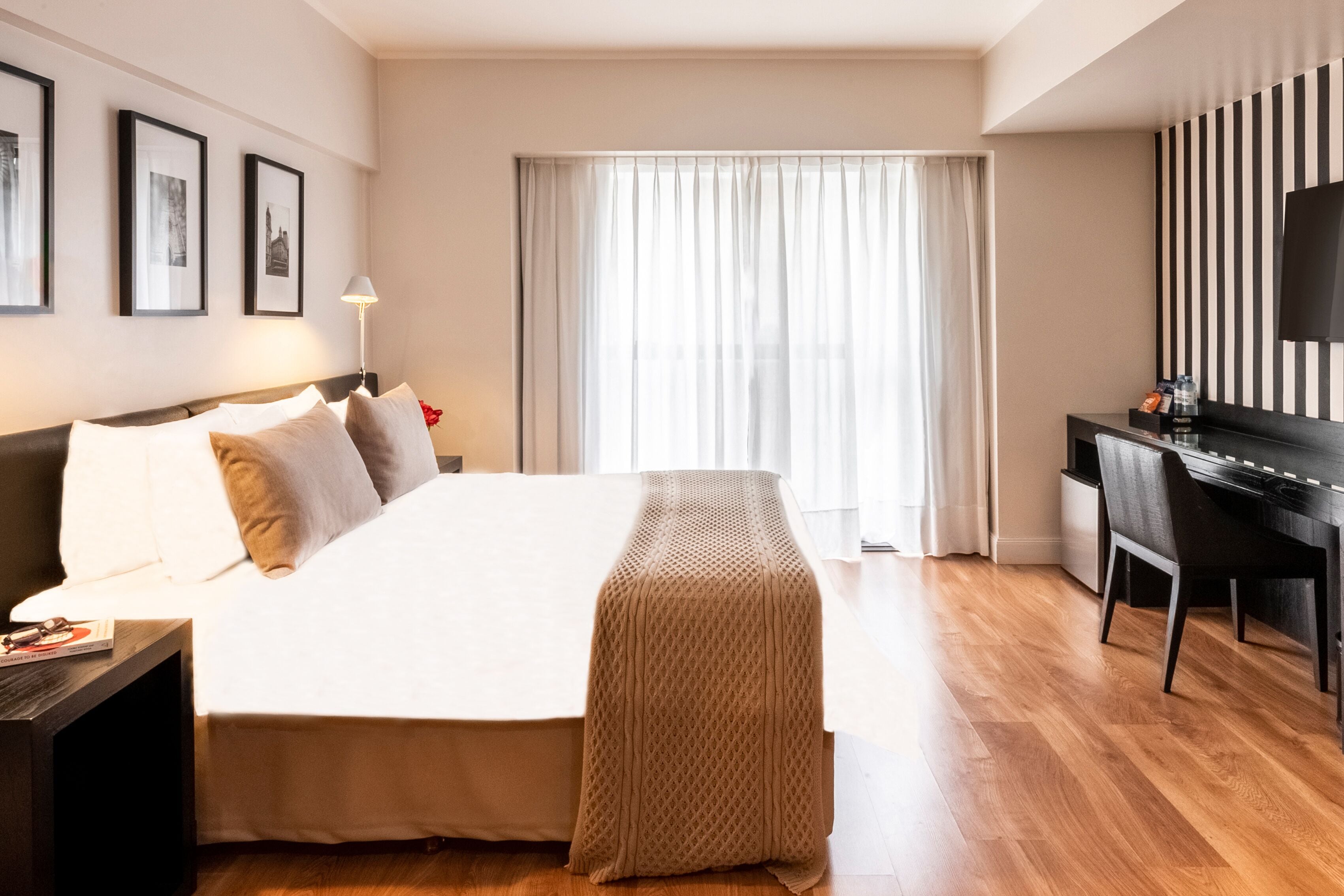 A hotel room with a large bed, a desk, a chair, a TV, and framed pictures on the wall.