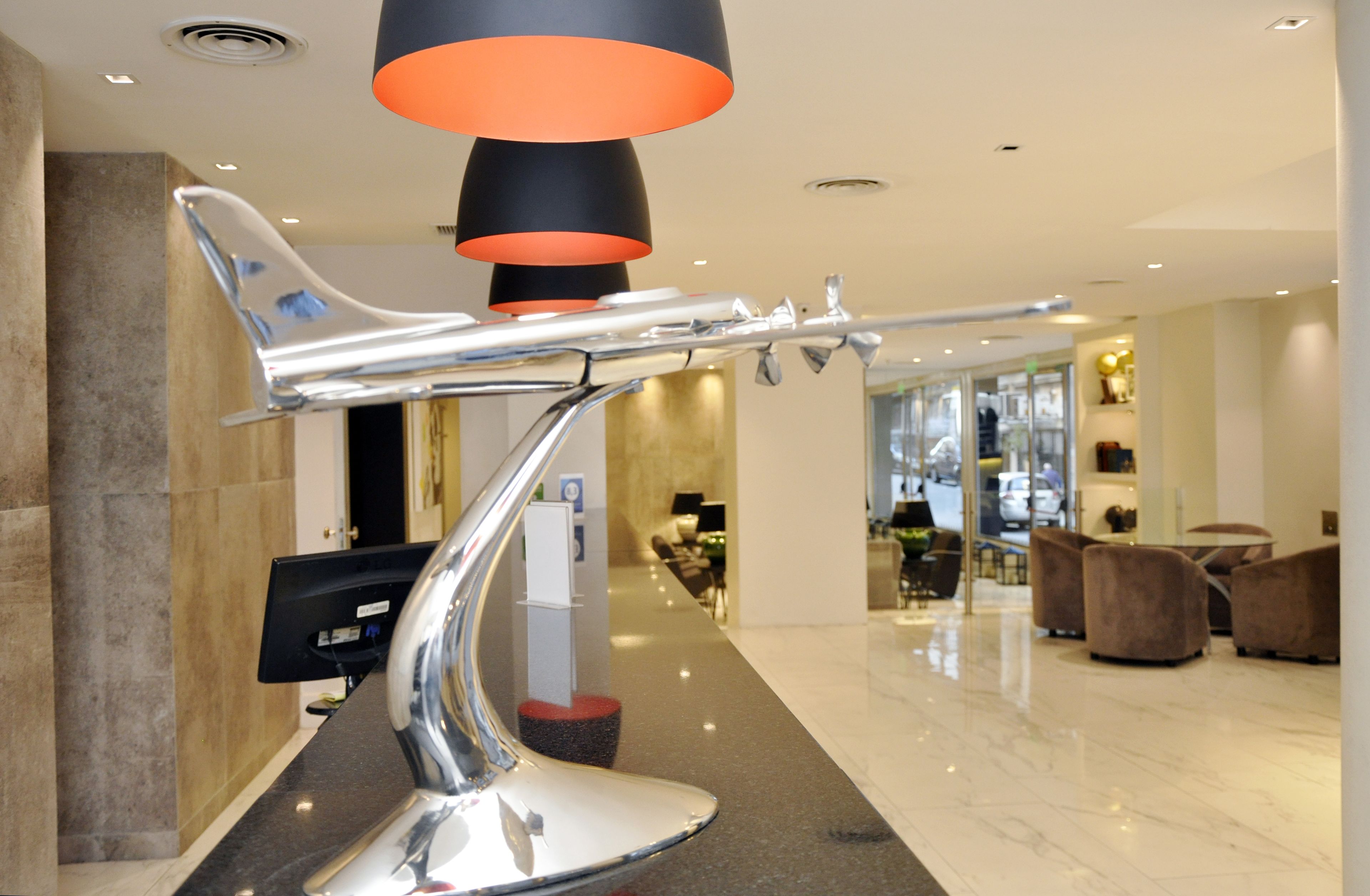 A modern lobby with a unique chrome sculpture, a reception desk, and a seating area with plush chairs.