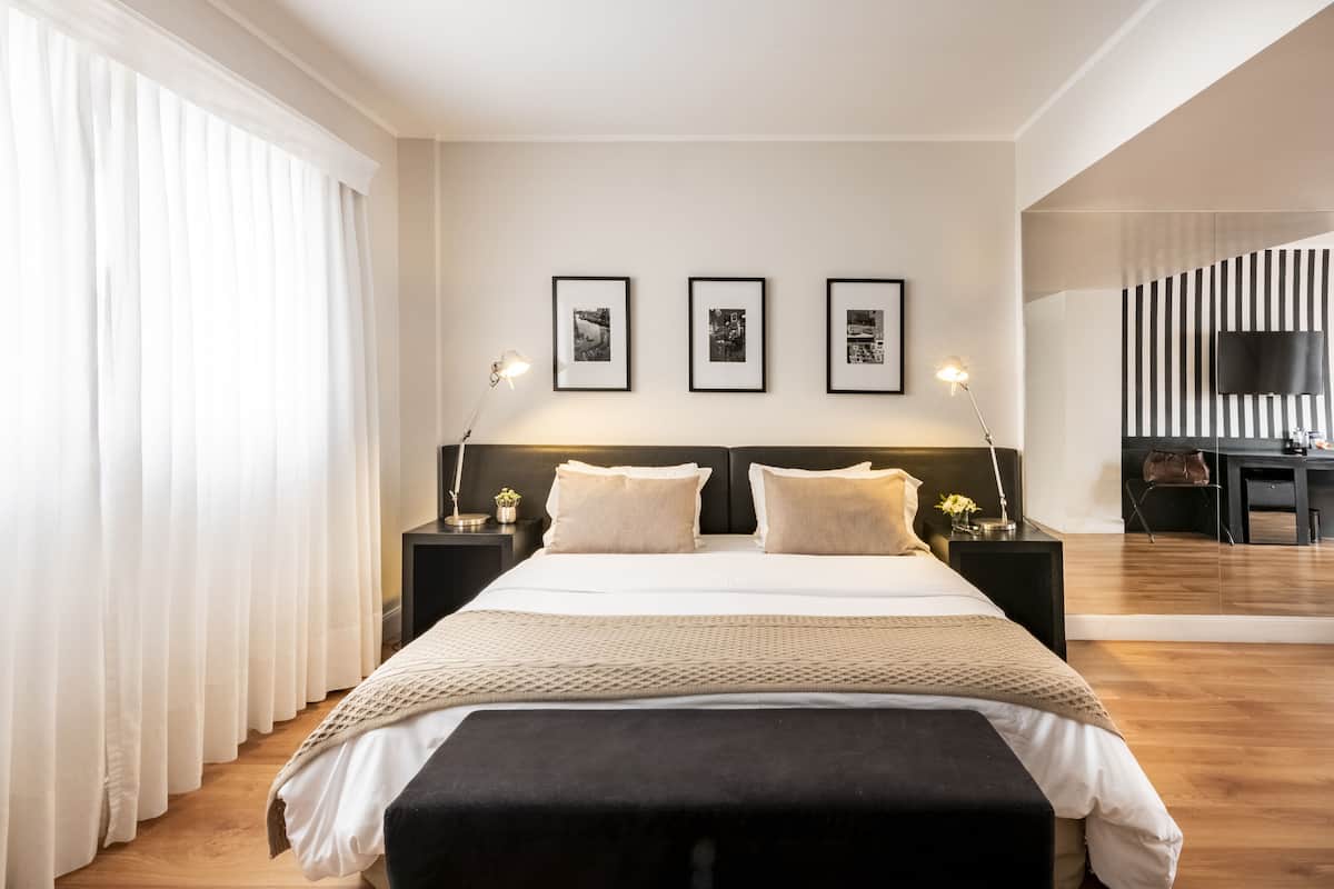 Una habitación de hotel moderna con una cama grande, dos mesitas de noche, un televisor de pantalla plana y tres cuadros enmarcados en la pared.
