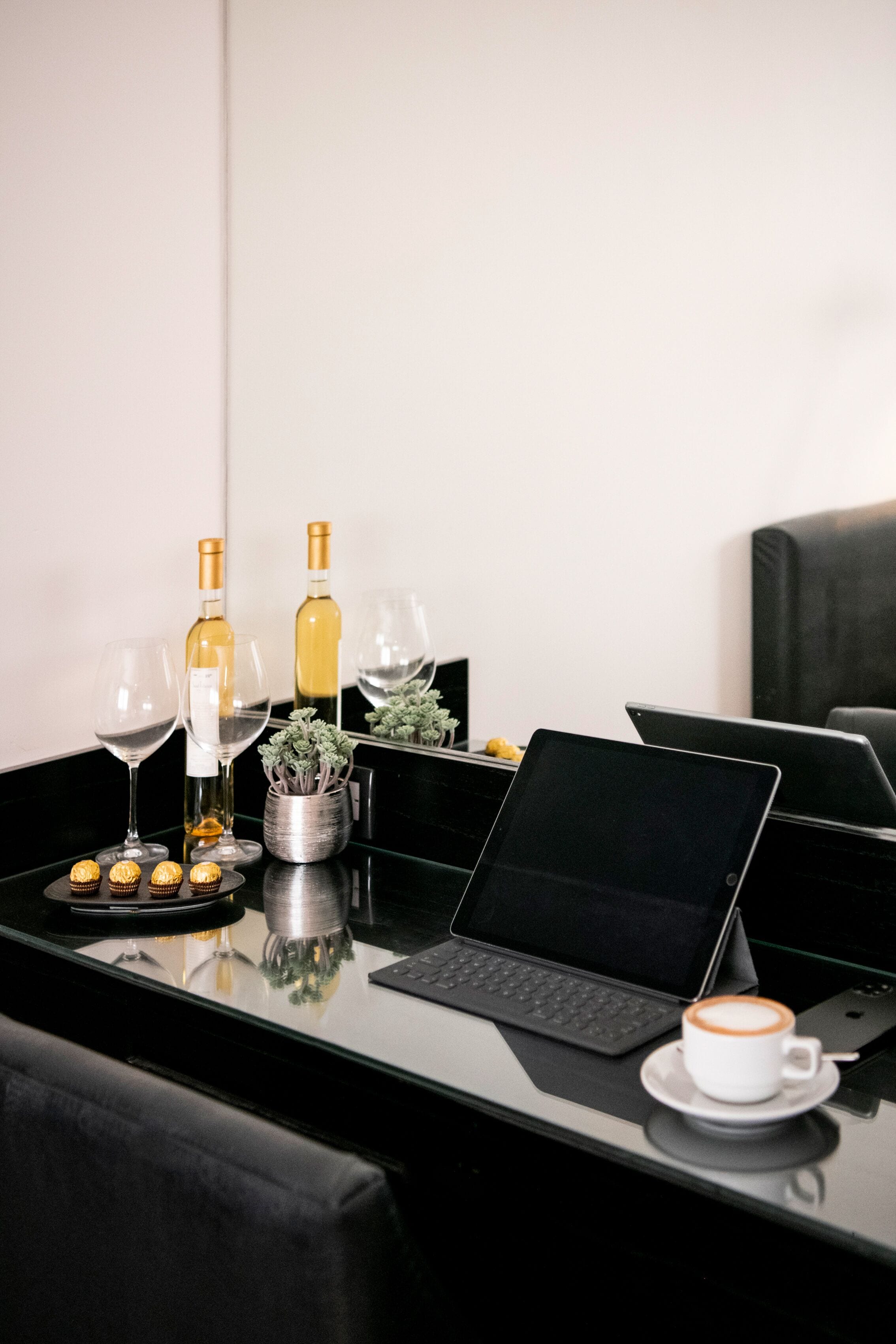 A modern workspace with two laptops, a coffee cup, wine glasses, and bottles on a glass table.