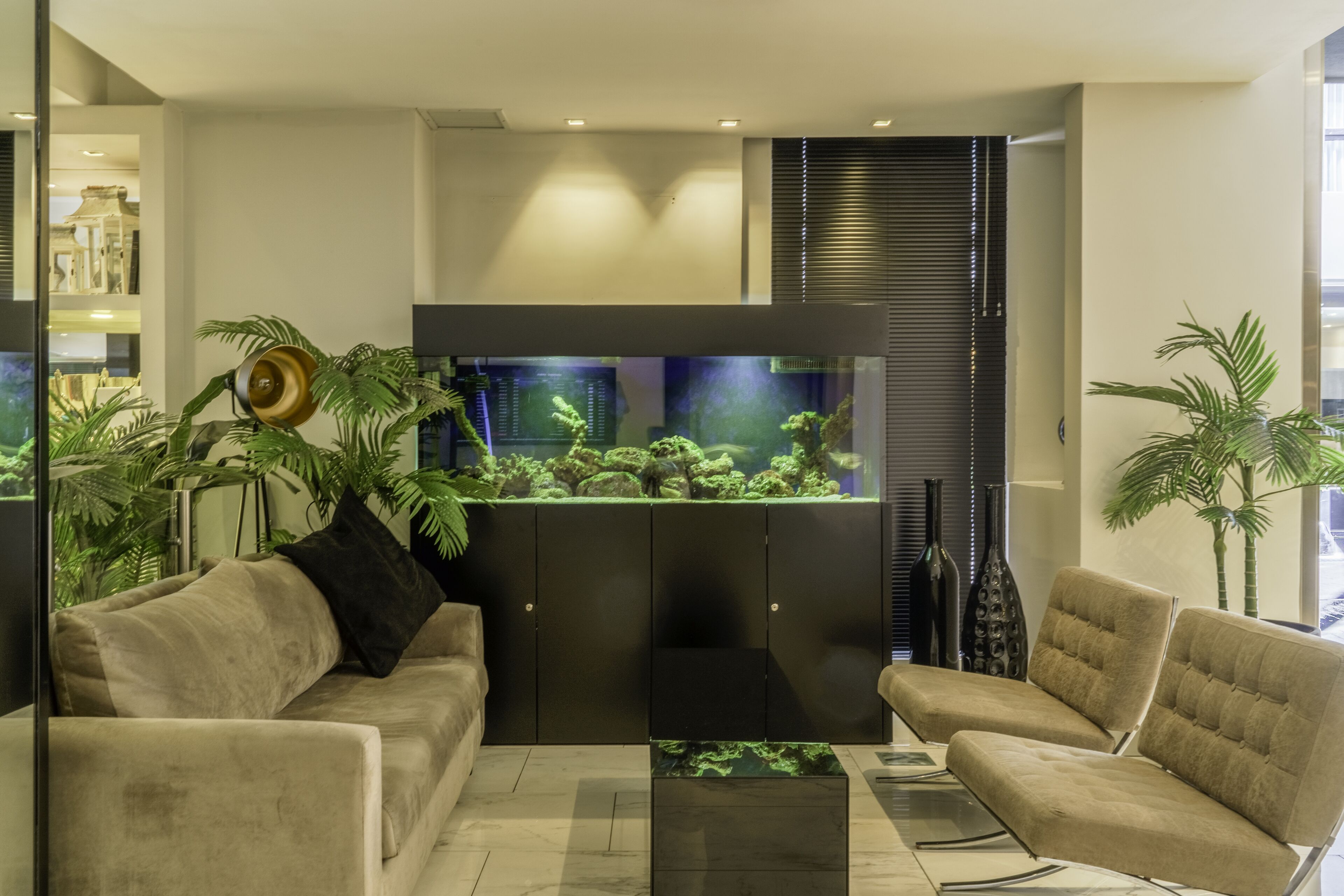 A modern living room with a large aquarium, comfortable seating, and decorative plants.