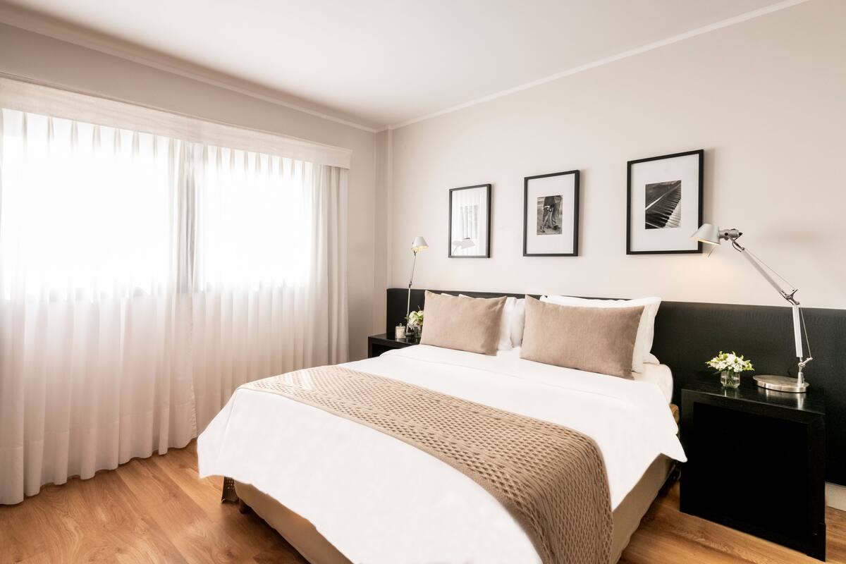 Habitación de hotel moderna con una cama grande, una mesita de noche con lámpara y tres cuadros en la pared.