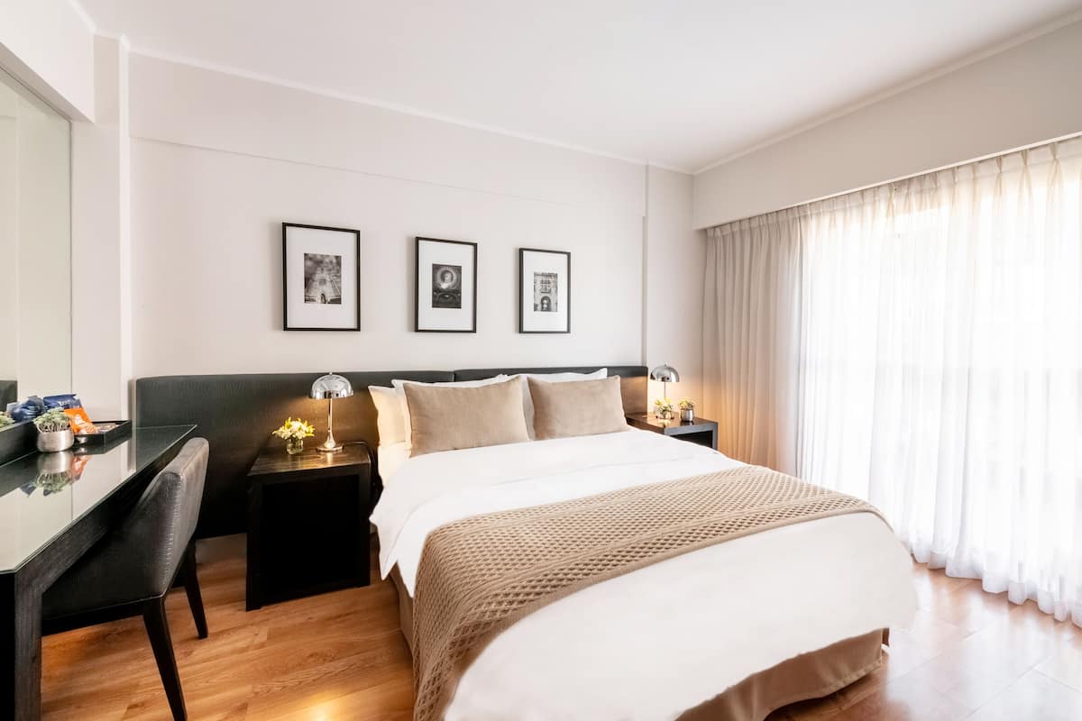 Habitación de hotel con una cama grande, un escritorio y dos cuadros en la pared.