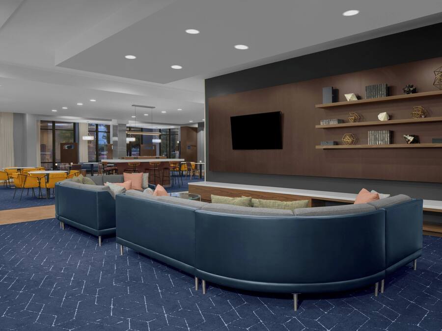 A modern lounge area with a curved blue sofa, a flat-screen TV mounted on the wall, and a bar area in the background.