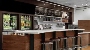 Eine moderne Bar mit einer weißen Arbeitsplatte, Metallhockern und Regalen voller Flaschen und Gläsern.