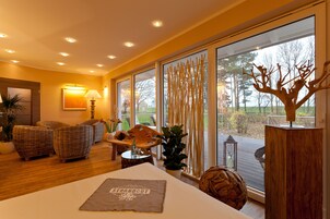 Ein modernes Wohnzimmer mit Korbmöbeln, einem Holztisch und einem großen Fenster mit Blick auf Bäume und einen Garten.