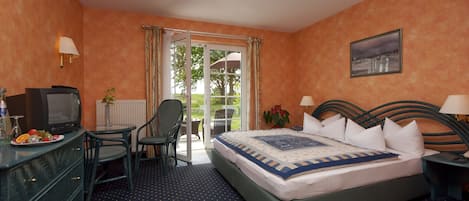 A hotel room with a bed, a desk with a computer, a chair, a television, and a view of the outdoors through a glass door.
