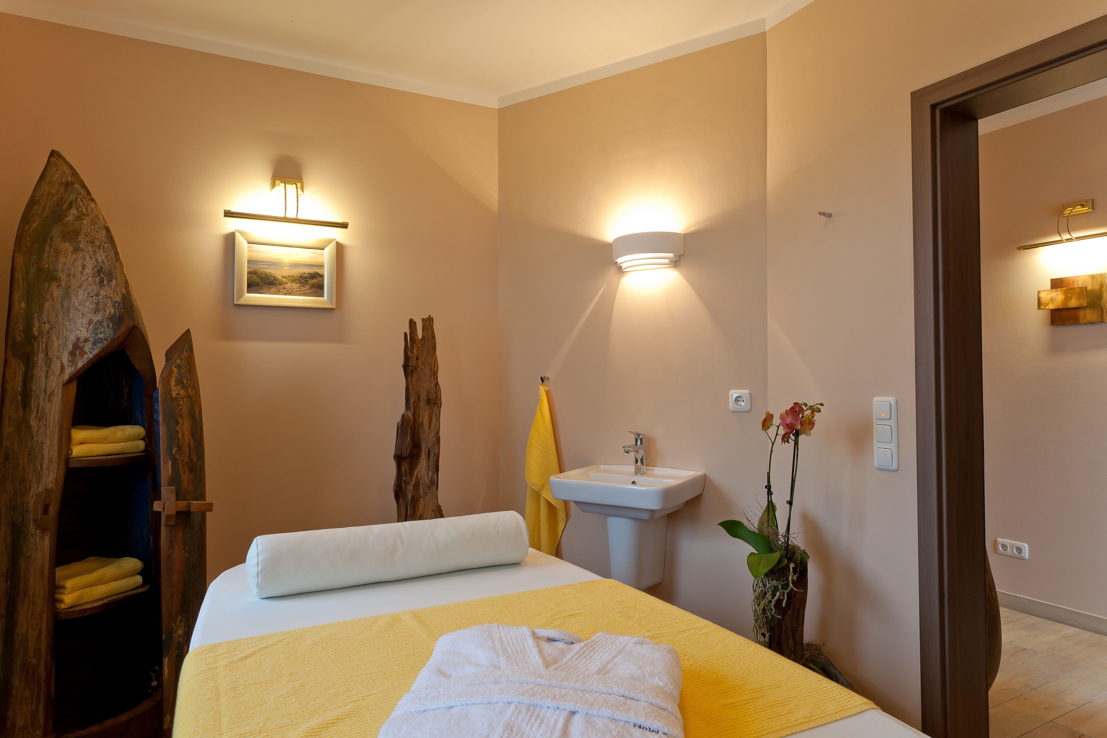 A hotel room with a bed, a wooden cabinet, a sink, and a wall-mounted light fixture.