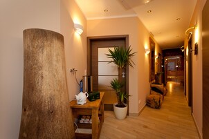Ein Korridor mit Holzboden, einer großen Holzsäule, einem Blumentopf, einem kleinen Tisch mit Teekanne und einer Tür mit Spiegel.