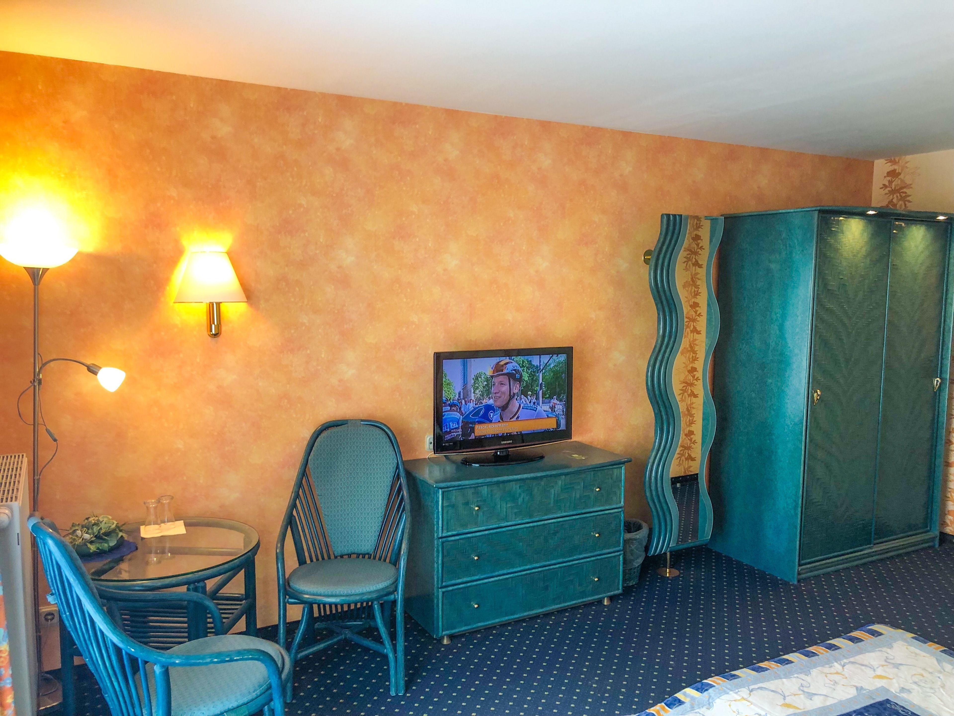 Ein Hotelzimmer mit Fernseher auf einer Kommode, einem Sessel, einem kleinen Tisch mit Gläsern und einem Kleiderschrank.