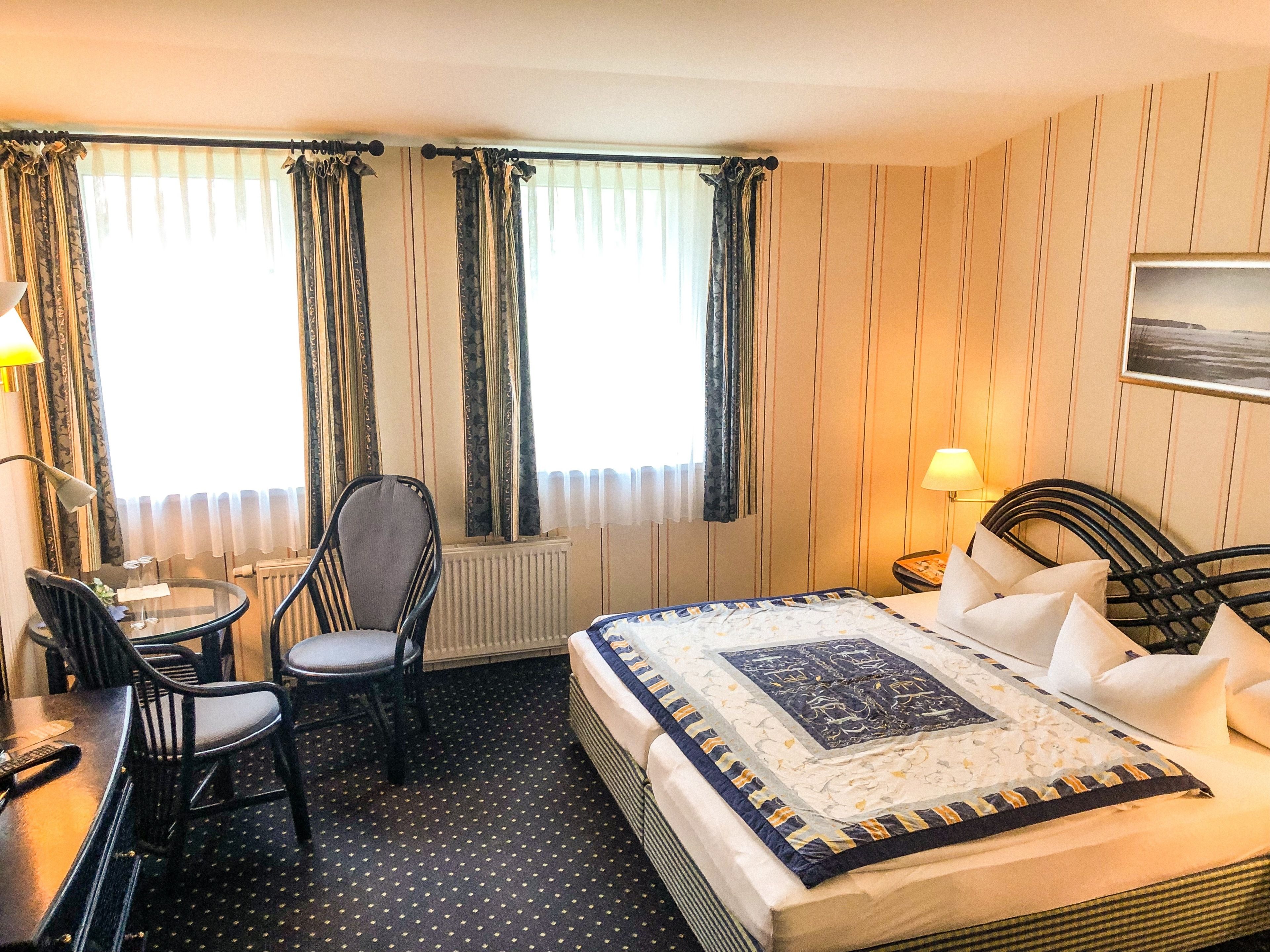 A hotel room with a bed, a chair, a small table, and a window with curtains.