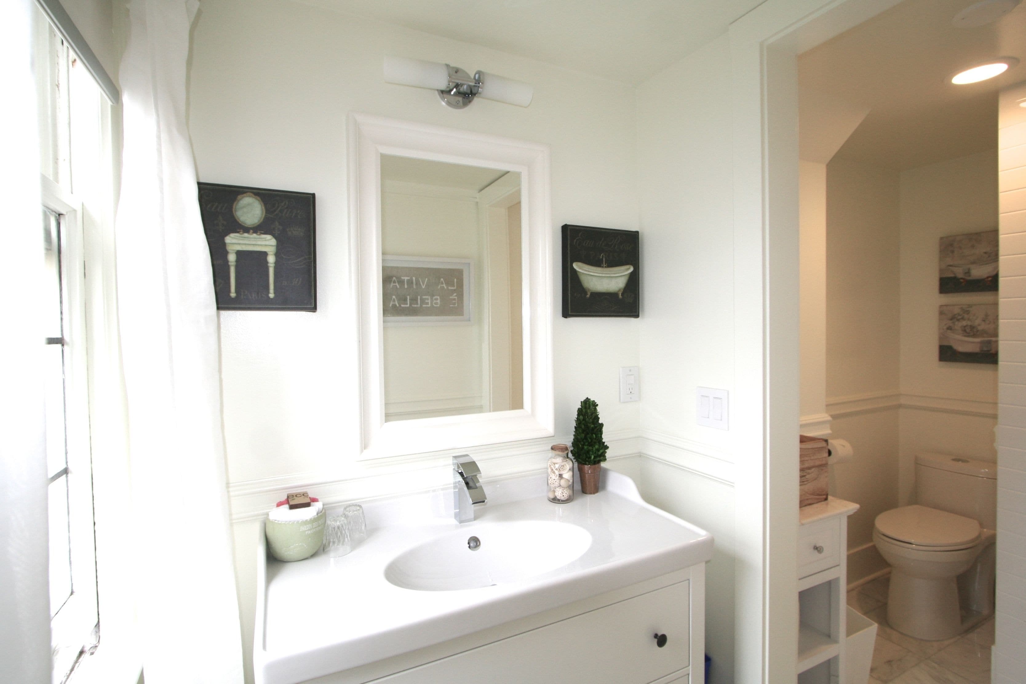 A bathroom with a white sink, mirror, and toilet. There are two framed pictures on the wall.