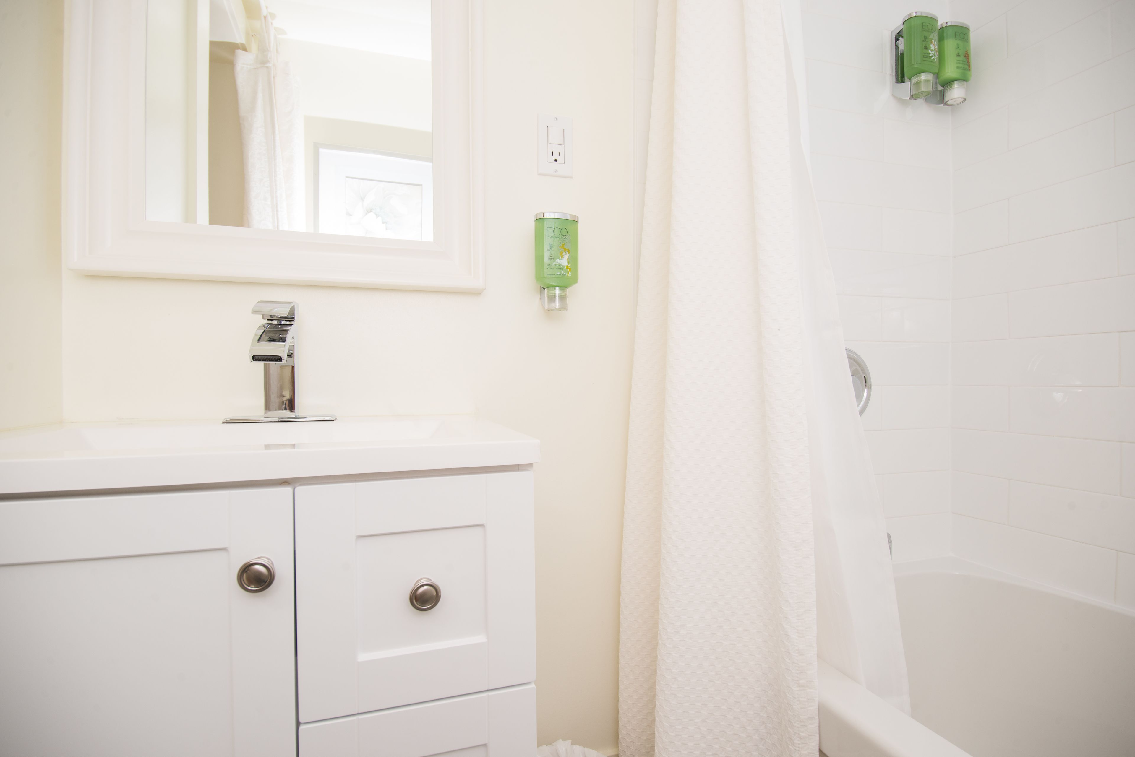 Een badkamer met een witte wastafel, spiegel en douchegordijn. Er staan groene toiletartikelen aan de muur.