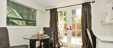 A room with a glass table, patterned chairs, a door with curtains, and a view of the outside.