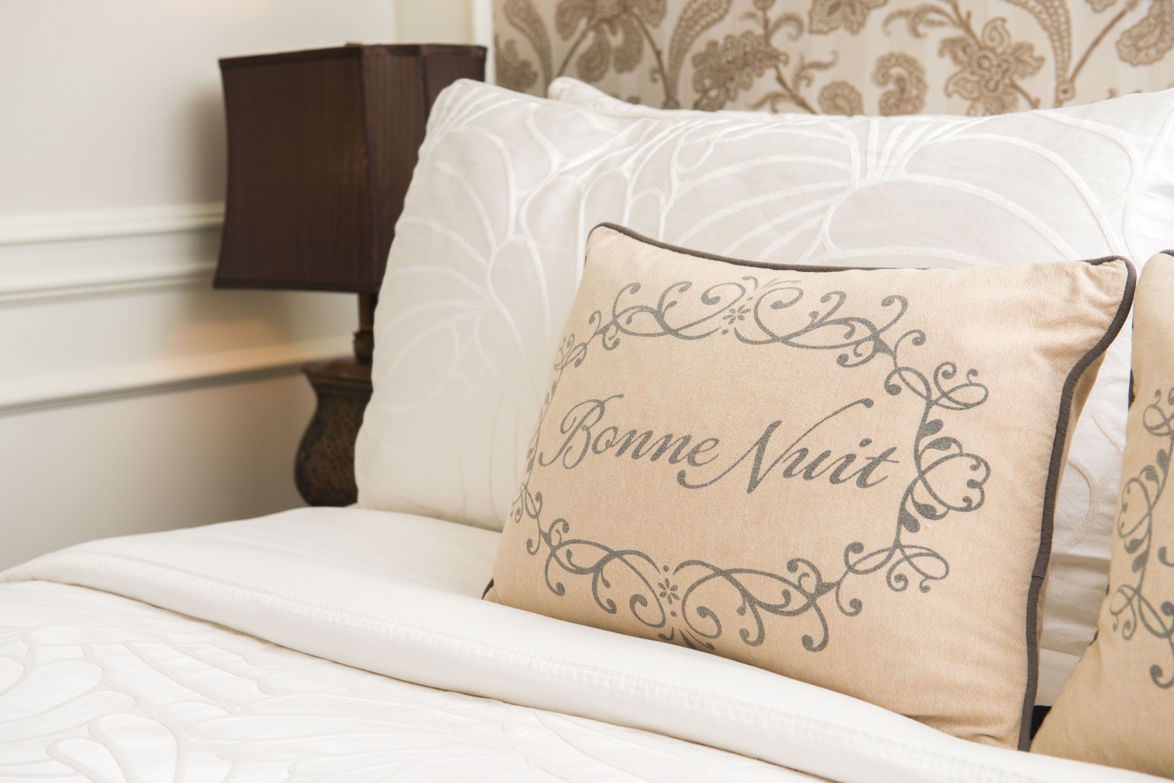 A bed with a beige pillow featuring decorative text and a white bedspread.