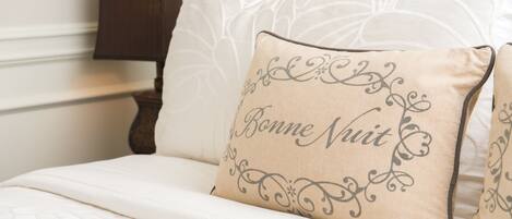A bed with a beige pillow featuring decorative text and a white bedspread.