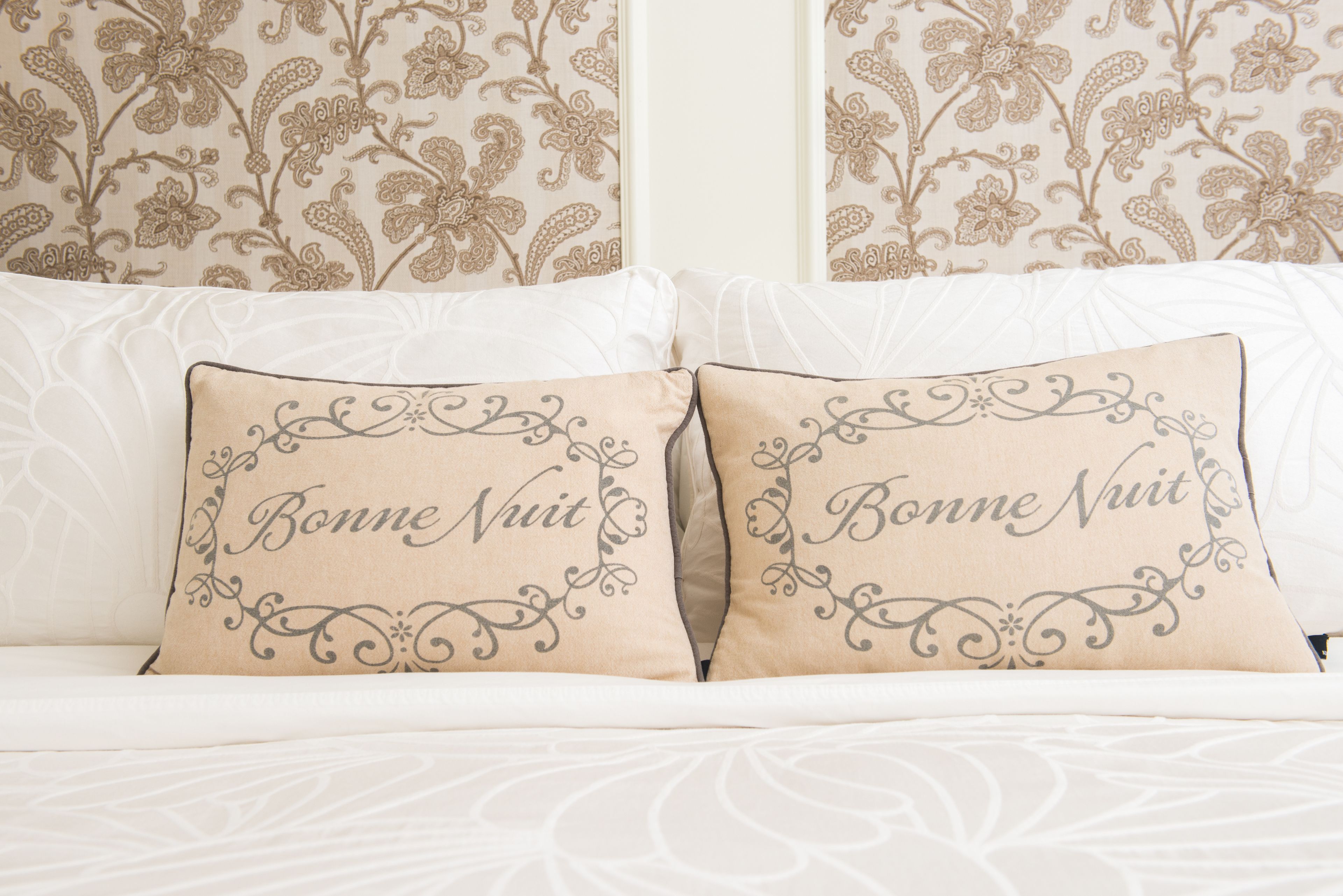 Un lit avec deux oreillers ornés de l’inscription « Bonne nuit » et un motif floral sur le mur situé derrière.