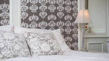 A neatly made bed with patterned pillows, a bedside lamp, and a wall with a floral wallpaper design.