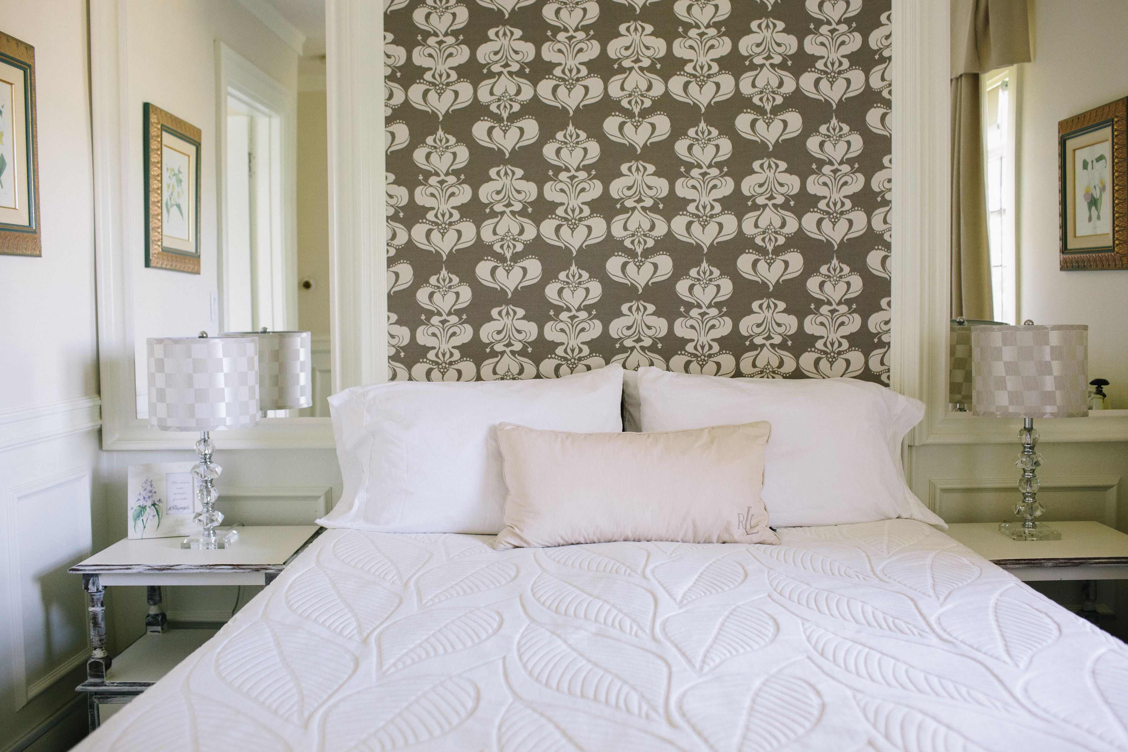 A hotel room with a large bed, two bedside tables, and a patterned wallpaper.