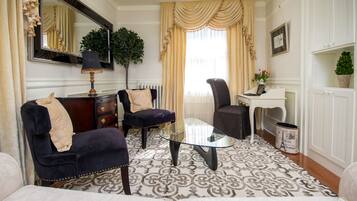 Un salon comprenant une table basse en verre, deux fauteuils, un canapé, une commode, un miroir, une plante en pot et un radiateur.